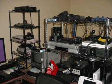 (Photo of my desk with a ridiculous 13-console 2 VCR A/V mega-setup.)